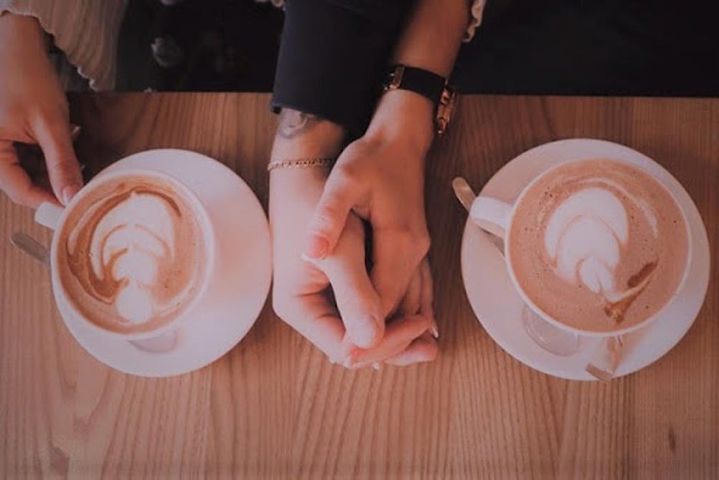 man and woman holding hands with coffee on the table